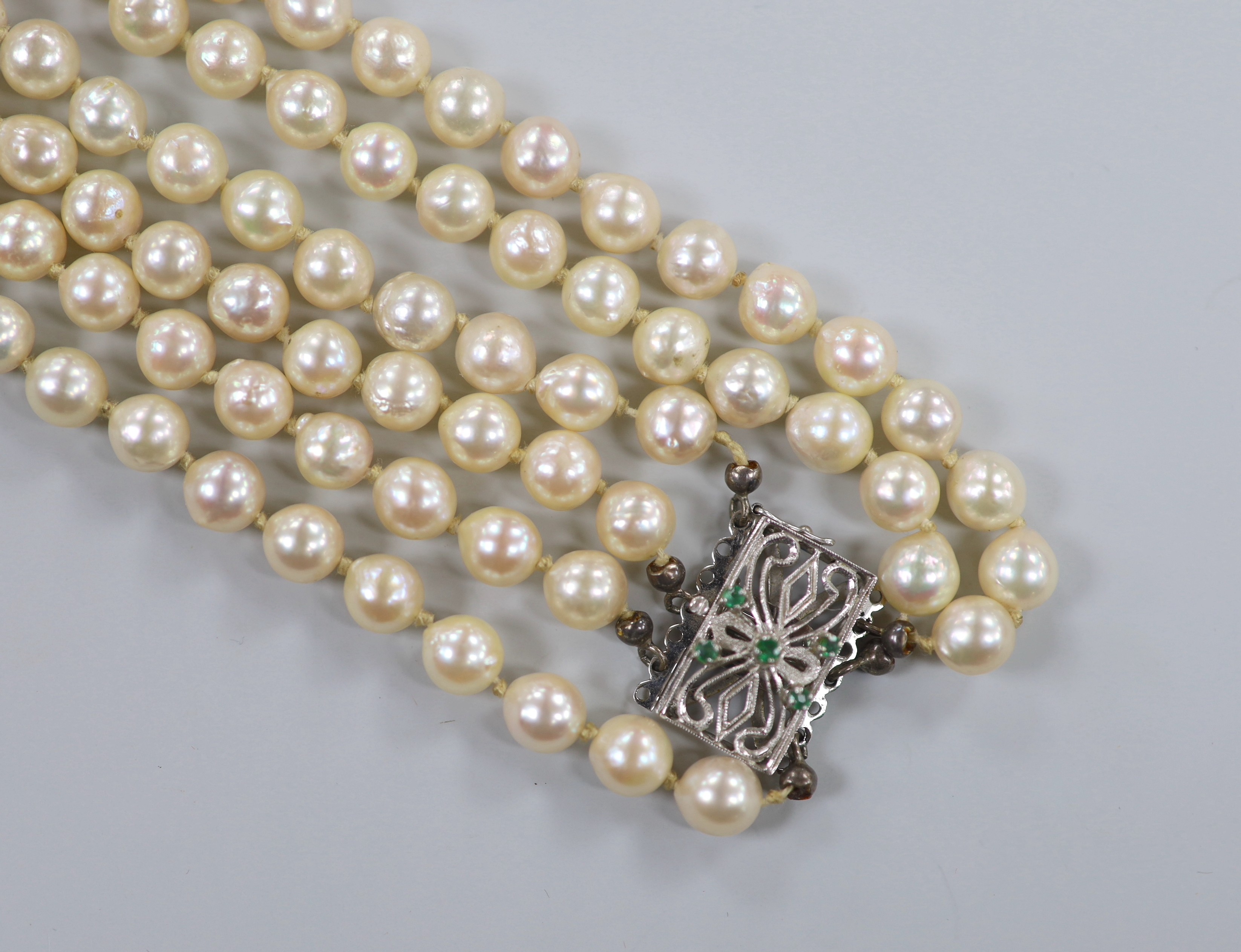 A mid to late 20th century triple strand cultured pearl necklace, with pierced 750 white metal and five stone emerald chip set clasp, approximately 56cm.